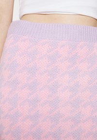 Primer plano de una falda de punto con patrón de pata de gallo en tonos lila y rosa, usada a la cintura, combinada con un top corto blanco.