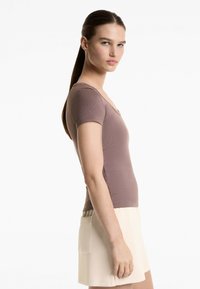 Top a maniche corte, aderente, di colore mauve tenue, realizzato in tessuto a costine. Design a V con una texture liscia. Abbinato a pantaloni corti beige.