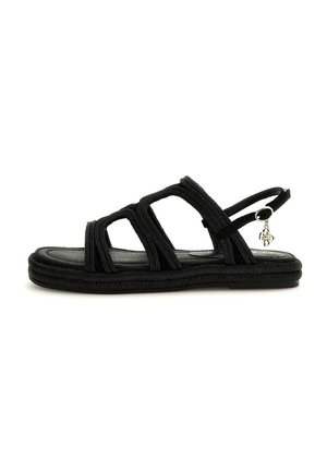Black flat sandal with three braided straps, ankle strap with silver buckle, and small hanging charm, shown on white background.
