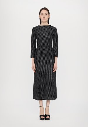 Vestido negro con lunares, de manga tres cuartos, cuerpo ajustado y falda fluida. Combinado con zapatos de plataforma negros con detalles de lazo.