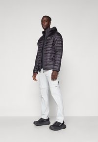 Black puffer jacket with horizontal baffle design, zip closure, and hood; paired with light gray cargo pants and black athletic shoes.