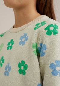 Stickad tröja i krämfärg med gröna och ljusblå blommönster. Har en rund halsringning och strukturerad tyg. Mjukt, lätt material.