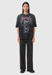 Zwarte grafische T-shirt met een schedelontwerp met slangen, korte mouwen, ontspannen pasvorm en een ronde halslijn, gecombineerd met donkere broek met wijde pijpen.