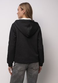 Czarna bluza z kapturem o fakturowanym wykończeniu, z błyszczącym wzorem, ściągaczami na mankietach i luźnym krojem, zestawiona z szarymi dżinsami.