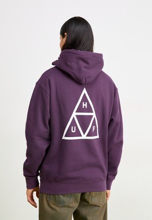 Haut à capuche violet avec un logo triangulaire blanc portant les lettres H, U et F. Matériel en coton doux, coupe oversize et poche kangourou à l'avant.