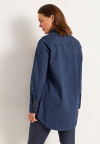 Tummansininen, pitkähihainen denim-paita, jossa on klassinen kaulus, napitettavat hihansuut ja kaareva helma.