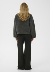 Grau melierter Wollpullover mit oversized Passform und überschnittenen Schultern, kombiniert mit hoch taillierten schwarzen Hosen, beide mit klaren Linien.
