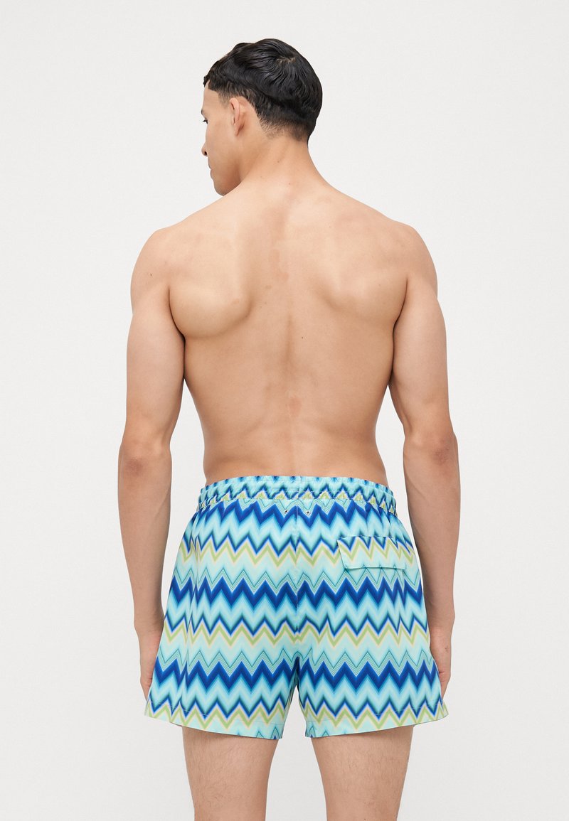 Costume da bagno con un motivo a zigzag in tonalità di blu e verde, dotato di una vita elastica e di una piccola tasca sul retro.