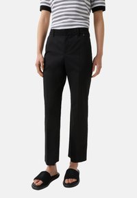 Pantalons noirs ajustés avec une coupe droite, dotés de poches avant et d'une texture lisse, associés à des sandales noires à glissière et un haut à rayures.