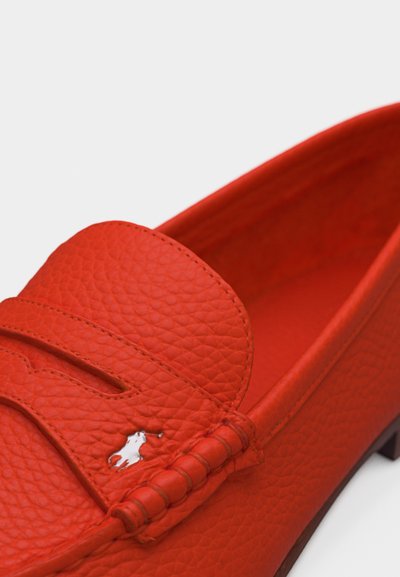 Κόκκινο μοκασίνι από δέρμα με υφή, με ραφές και μικρό μεταλλικό λογότυπο με άλογο και αναβάτη στο μπροστινό μέρος.
