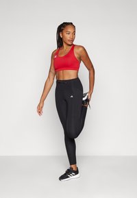Sostenedor deportivo rojo y leggins negros de cintura alta hechos de tela elástica; presenta una textura suave y un ajuste entallado. Acabado con un logo blanco.