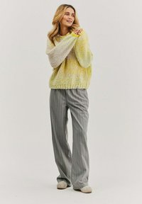 Pletený sveter v žltej a levanduľovej farbe; voľný strih s balónovými rukávmi. Kombinovaný so šedými prúžkovanými nohavicami a svetlošedou obuvou.