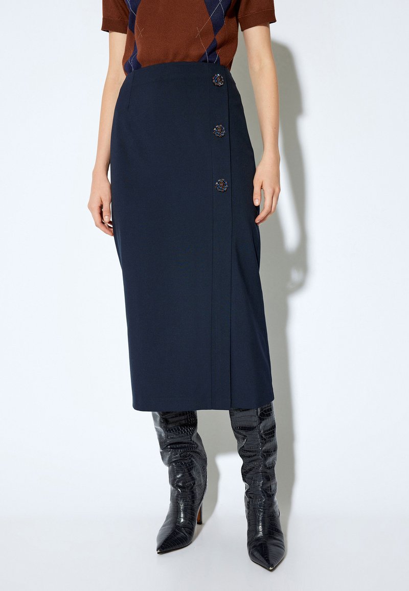Jupe crayon bleu marine en tissu lisse, ornée de trois boutons décoratifs sur le côté et d'une silhouette élégante et épurée.