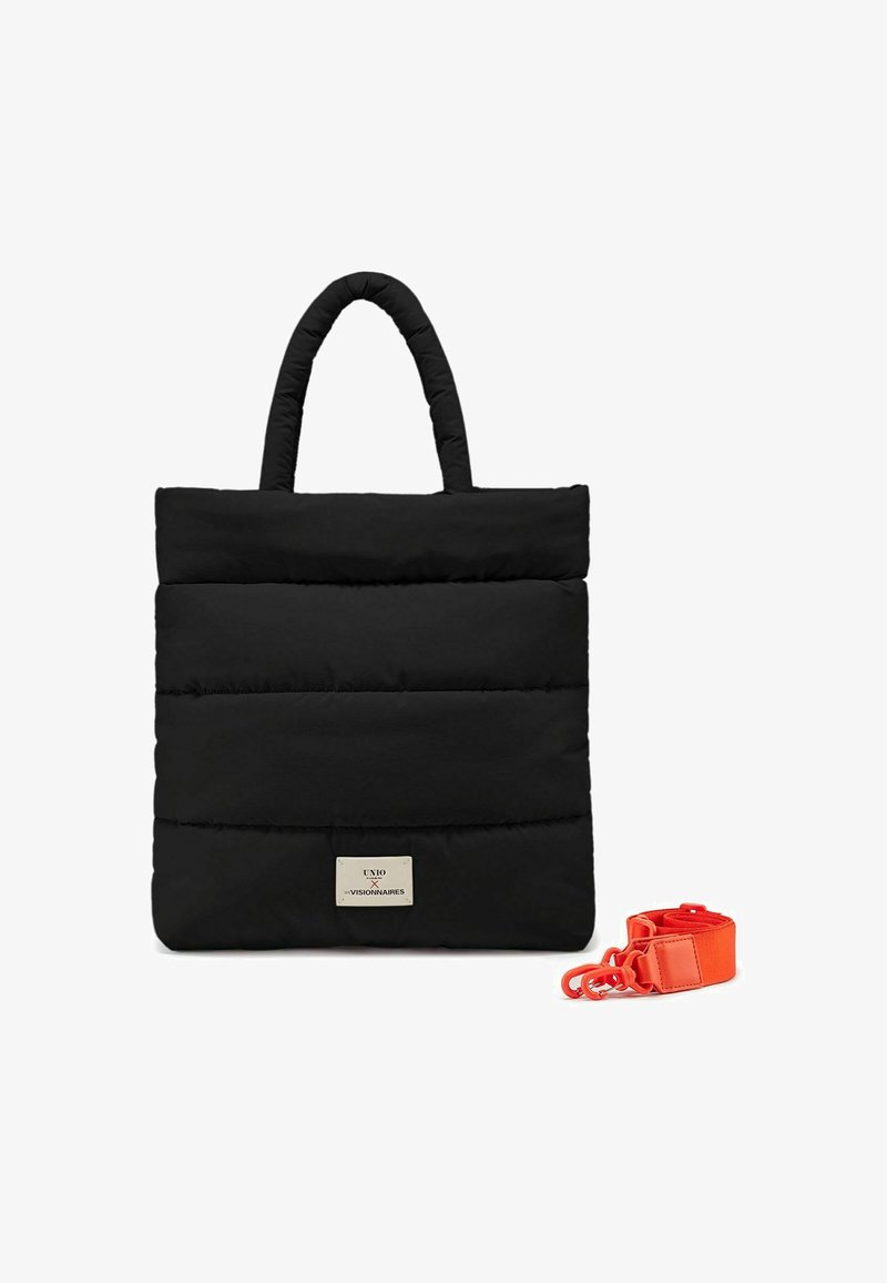 Sac fourre-tout noir rembourré avec deux poignées, présentant une plaque logo dorée et une sangle amovible orange sur le côté. Texture lisse, design minimaliste.
