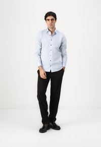 Svijetloplava košulja s dugim rukavima, tamni gumbi, prilagođenog kroja, uparena s crnim hlačama i elegantnim crnim cipelama.