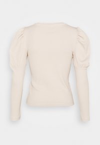 Haut à manches longues en tissu côtelé beige clair, avec des épaules bouffantes et une silhouette ajustée, col rond.