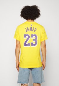 Gul bomullst-shirt med korta ärmar, med "JAMES" och numret "23" i lila på baksidan. Casual design med avslappnad passform.