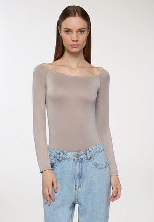 Body a maniche lunghe in taupe chiaro, design off-shoulder con una texture liscia. Abbinato a jeans blu scoloriti a vita alta.