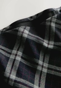 Schwarz-grauer karierten Stoff mit einer weichen Textur, der ein geometrisches Karomuster und subtile rote Akzente aufweist, drapiert und teilweise gefaltet.