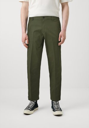Olive green cotton trousers with a straight fit, front pockets, a button closure, and a smooth texture. Paired with black high-top sneakers.