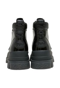 Bottines en cuir verni noir avec semelles épaisses, ornées d'accents de logo embossés et d'une languette pour un enfilage facile. Texture lisse, design minimal.