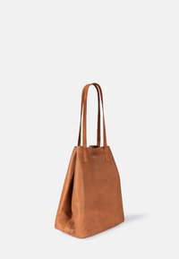 Braune Leder-Totetasche mit verlängerten Trägern, strukturierter Oberfläche und dreieckiger Form, die ein minimalistisches Design ohne sichtbare Beschläge aufweist.