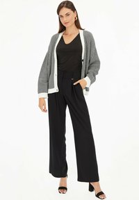 Czarne szerokie spodnie z wysokim stanem, w połączeniu z czarnym topem o dekolcie w serek oraz wzorzystym kardiganem w czarno-białe motywy z dużymi rękawami.