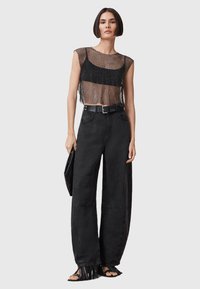 Czarny siatkowy crop top nałożony na czarną bluzkę na ramiączkach, połączony z czarnymi spodniami o wysokim stanie i szerokich nogawkach. Zawiera pasek i sandały z frędzlami.