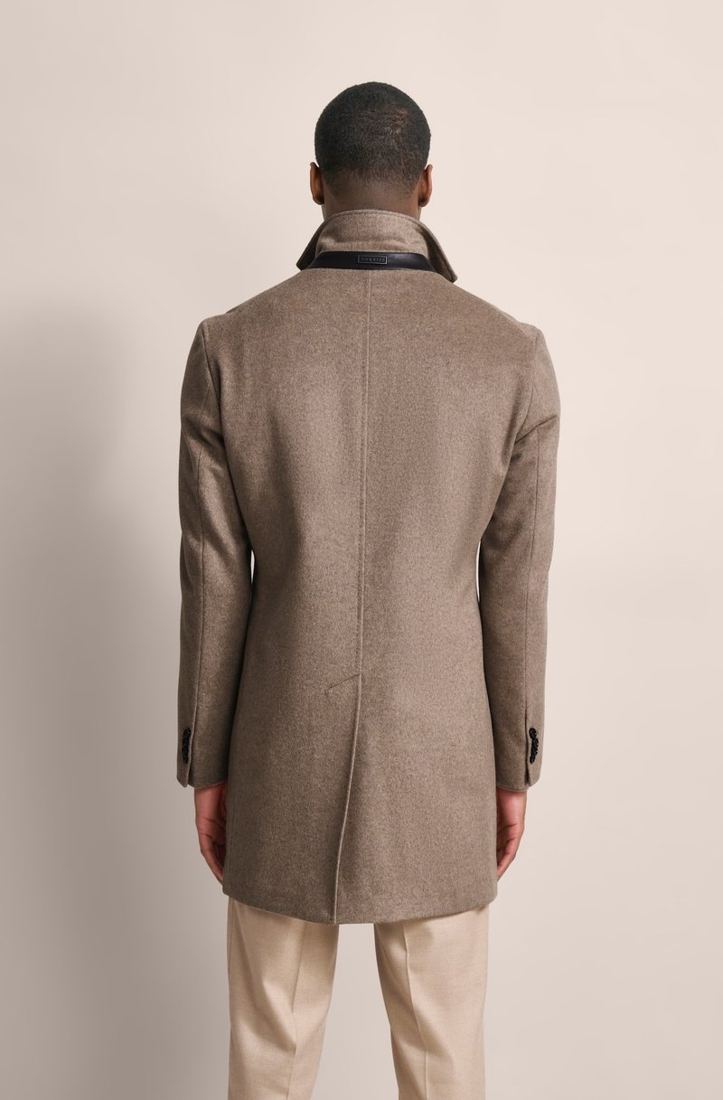 Cappotto di lana marrone con colletto alto, apertura centrale e polsini con bottoni. Presenta una texture liscia e linee pulite.