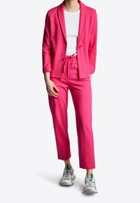 Vaaleanpunainen bleiseri ja siihen sopivat housut pehmeästä kankaasta; bleiserissä on huopakaulus ja yksittäinen nappi, housuissa on joustava vyötärö ja nauha.