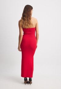 Rotes geripptes, gestricktes, trägerloses Midikleid, figurbetont mit geradem Schnitt. Getragen mit schwarzen High Heels. Die Rückansicht zeigt eine glatte Textur.