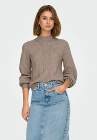 Maglione marrone in knit testurizzato con collo alto e polsini a coste, abbinato a una gonna a tubino in denim chiaro con chiusura frontale a bottoni e tasche.