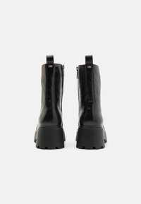 Botas de tobillo de cuero negro con una suela de goma gruesa, que cuentan con una cremallera lateral y una lengüeta en la parte superior, exhibiendo un acabado texturizado.