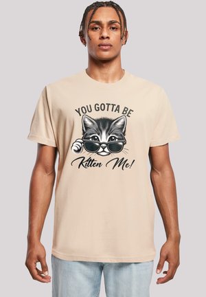 Beige cotton t-shirt featuring a graphic of a cat in sunglasses with the text "YOU GOTTA BE KITTEN ME!" in black below the image.