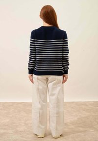 Granatowy sweter w paski z białymi poziomymi paskami, okrągły dekolt, noszony z kremowymi spodniami o szerokich nogawkach, z ribbowanymi mankietami i dołem.