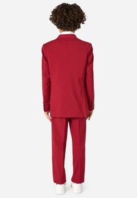 Completo bordeaux con blazer strutturato e pantaloni su misura. Tessuto liscio con cuciture minime, abbinato a sneaker bianche. Elementi di design semplici.