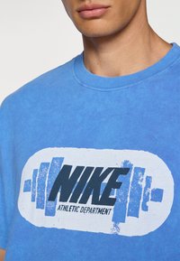Blå bomulds T-shirt med rund hals og et falmet tryk, der viser teksten "NIKE" og "ATHLETIC DEPARTMENT" sammen med vægtstænger.