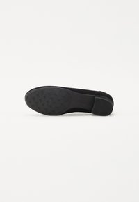 Zapato de tacón negro de gamuza con punta redonda, suela de goma texturizada y tacón bajo cuadrado. Presenta un upper suave y un logotipo sutil en la suela.