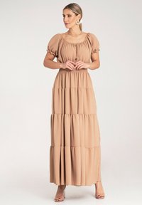 Maxi sukienka z jasnobeżowego materiału, z kwadratowym dekoltem, krótkimi bufkami i detalami w postaci guzików, z falbanami w poziomie u dołu.
