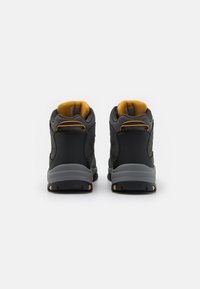 Scarpe outdoor alte nere con accenti grigi e foderatura gialla. Presentano un tessuto testurizzato e una suola robusta con punte di trazione.