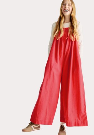 Rode linnen jumpsuit met wijde benen, geplooide taille en zijzakken, gecombineerd met beige sneakers. Glad textuur, casual ontwerp.