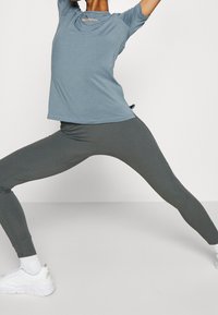 T-shirt de sport bleu clair et leggings verts foncés. Le t-shirt a un col rond et des manches courtes, tandis que les leggings sont ajustés avec une texture lisse.