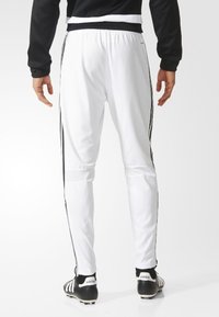 Vita träningsbyxor med svarta sidosträck, elastisk midja och smalnande ben, tillverkade av lättviktigt material, lämpliga för sportaktiviteter.