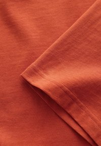 Bomulds T-shirt i en dæmpet terracotta farve med en glat tekstur, der har en ren kant og foldet ærmedetalje.