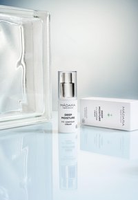 Crème contour des yeux Mádara Deep Moisture dans un flacon transparent avec des accents argentés à côté d'une boîte blanche affichant les informations sur le produit.