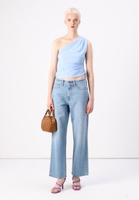 Top azul claro de un solo hombro, con diseño arrugado, combinado con unos vaqueros de pierna ancha y cintura alta en azul claro. Sosteniendo un pequeño bolso marrón, con tacones morados.