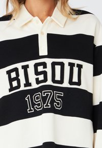 Black and white striped polo shirt with a buttoned collar, featuring "BISOU" and "1975" embroidered in bold black lettering.