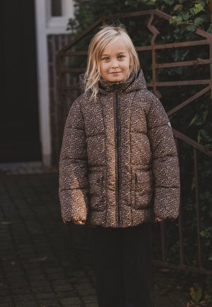 Pufferjack met een bruin en zwart luipaardprint, voorzien van een capuchon, een ritssluiting aan de voorkant en twee voorzakken. Kind dat buiten staat.
