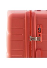 Koraalroze harde koffer met dubbele ritssluiting, combinatieslot en getextureerde groeven voor grip. Metalen accenten zichtbaar.