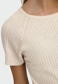 Jasno beżowa bluzka z krótkim rękawem, uszyta z prążkowanej dzianiny. Charakteryzuje się okrągłym dekoltem i delikatnym połyskiem, z poziomymi paskami na całej powierzchni.
